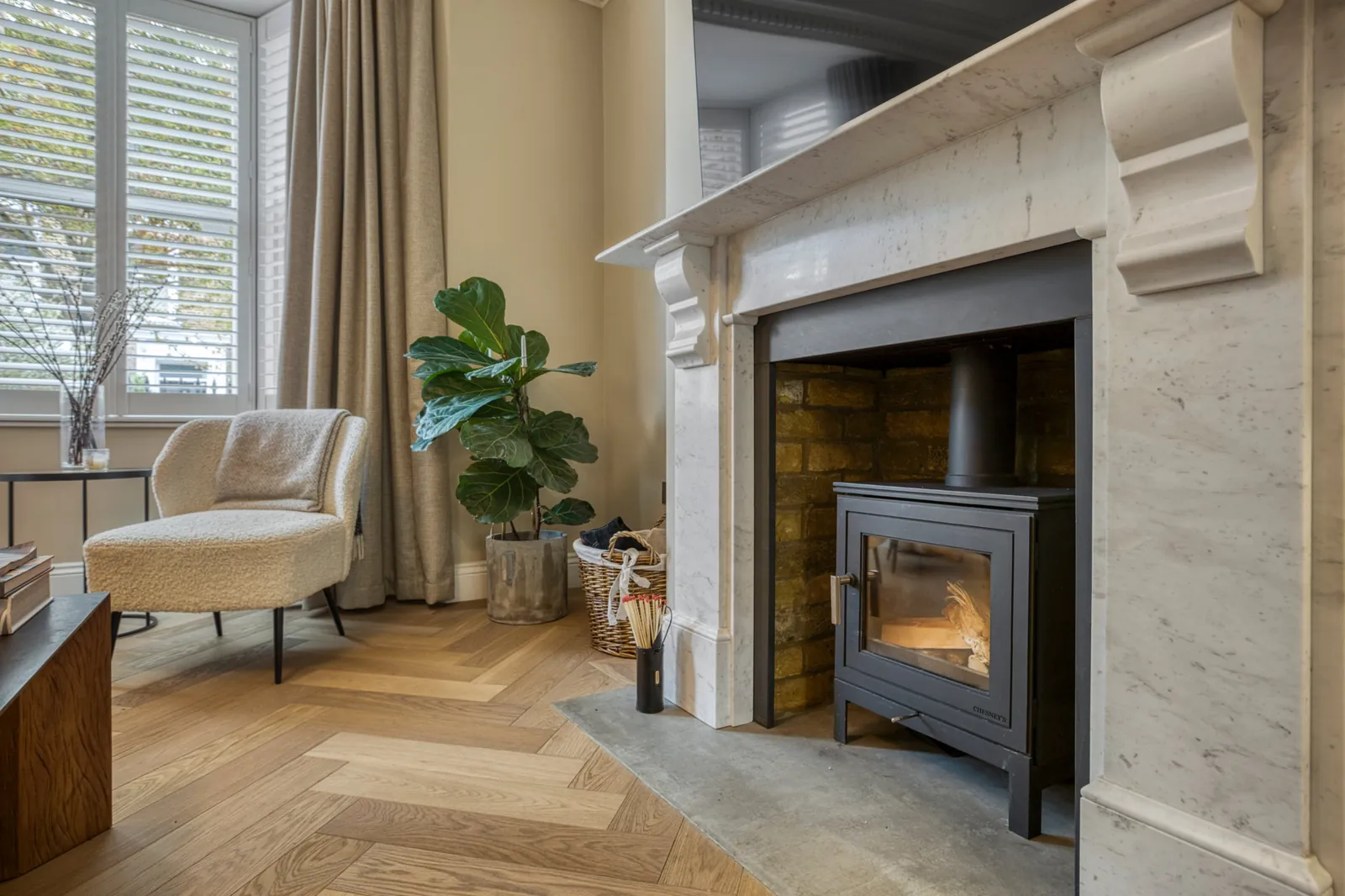 Living room with a marble fireplace, wood burner, herringbone oak floor and shuttered windows