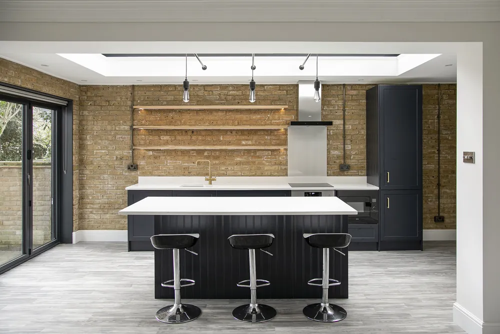 Kitchen in a Fulham rear extension with a lantern rooflight, exposed brick and a navy island