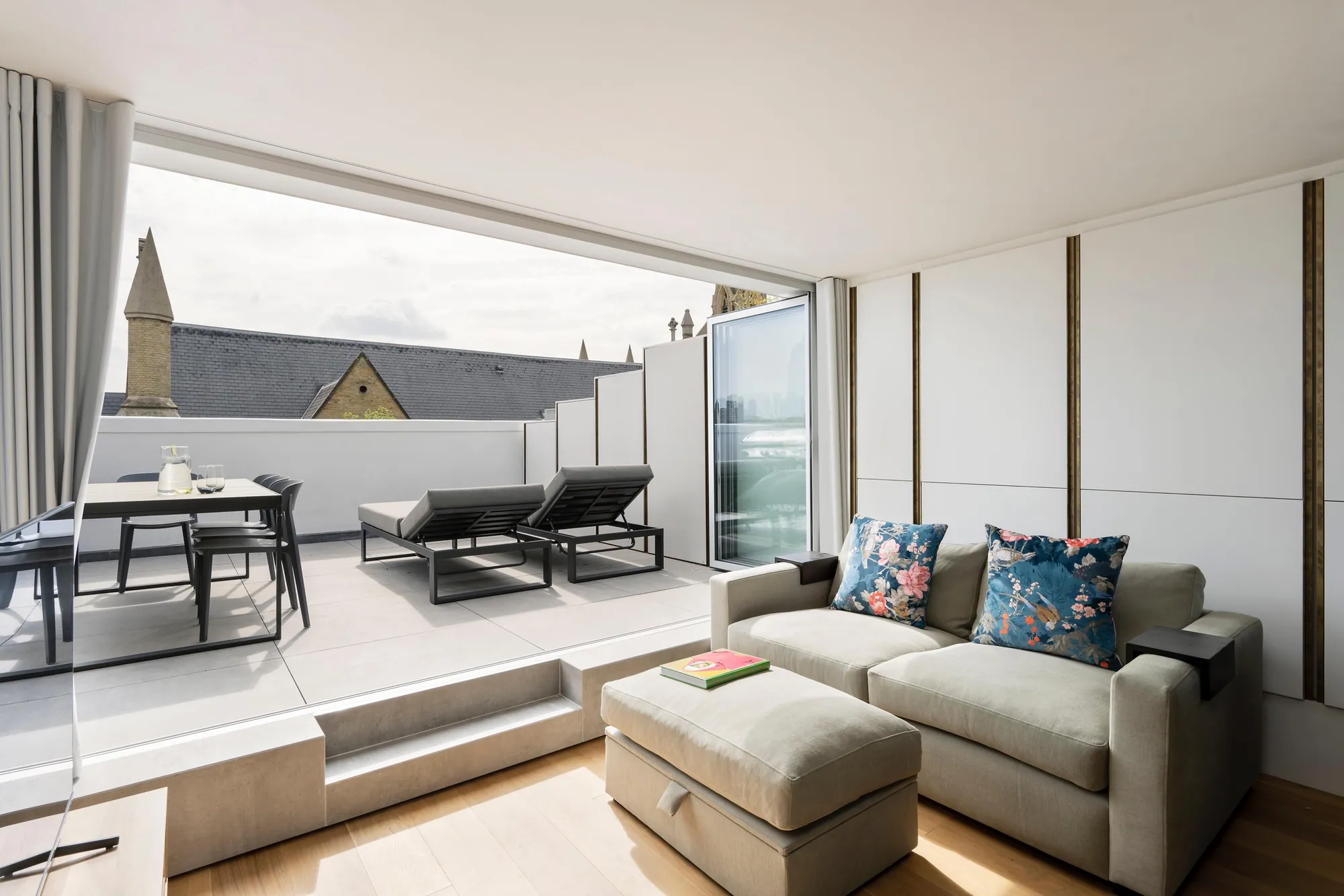 Top-floor living room in Islington opening onto a roof terrace through wide glazing, with London rooftops beyond