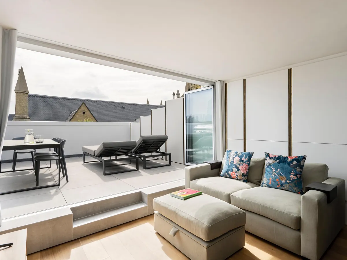 Top-floor living room opening onto a roof terrace through wide sliding glazing, with London rooftops beyond